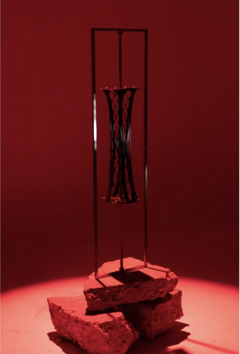 Threaded Rod Mechanism Iteration 2 - black woven hourglass form suspended in a steel frame atop stacked concrete, lit in red